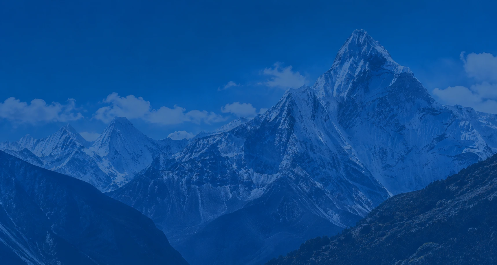 Snow-capped mountain peaks with a blue overlay under a clear sky.