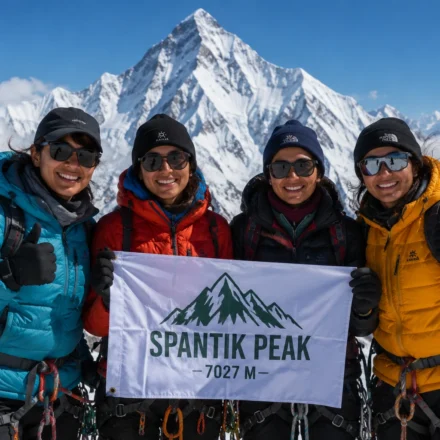 Four women mountaineers from Gilgit-Baltistan pose on the snow-covered summit of Spantik Peak, holding a Pakistani flag.